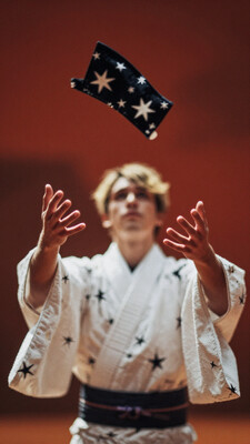 1boy, male focus, depth of field, film grain, surreal, red background, outstretched hand, long sleeves, sidelighting, reaching, blurry background, black eyes, blurry, upper body, kimono, obi, floating, collared jacket, fingernails, reaching towards viewer, jacket on shoulders, wide sleeves, white kimono, limited palette, facing viewer, brown background, sash, blurry foreground, orange theme, blonde hair, shirt, star print, looking up, japanese clothes, solo, jacket, black jacket, floating object, floating hair, from side, star \(symbol\), short hair, profile, abstract background, covered face, hands up, white shirt